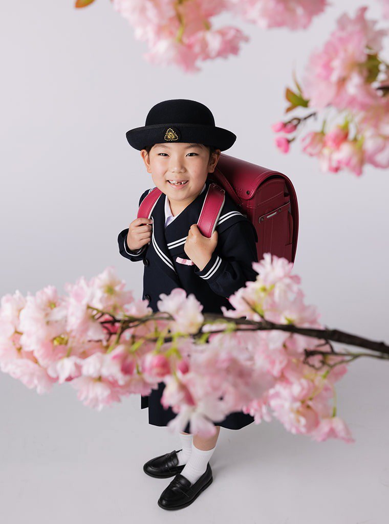 写真:桜の花とランドセルを背負った小学校入学の女の子